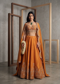 Woman in an orange traditional outfit with intricate designs standing against a neutral background.