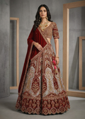 Woman in a traditional maroon and gold embroidered outfit standing against a gray wall.