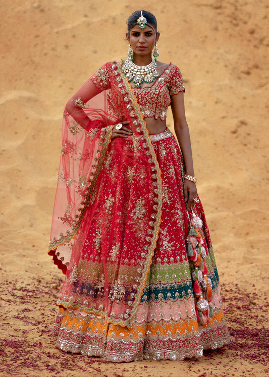 Woman in traditional red and multicolored embroidered outfit with jewelry against a desert background