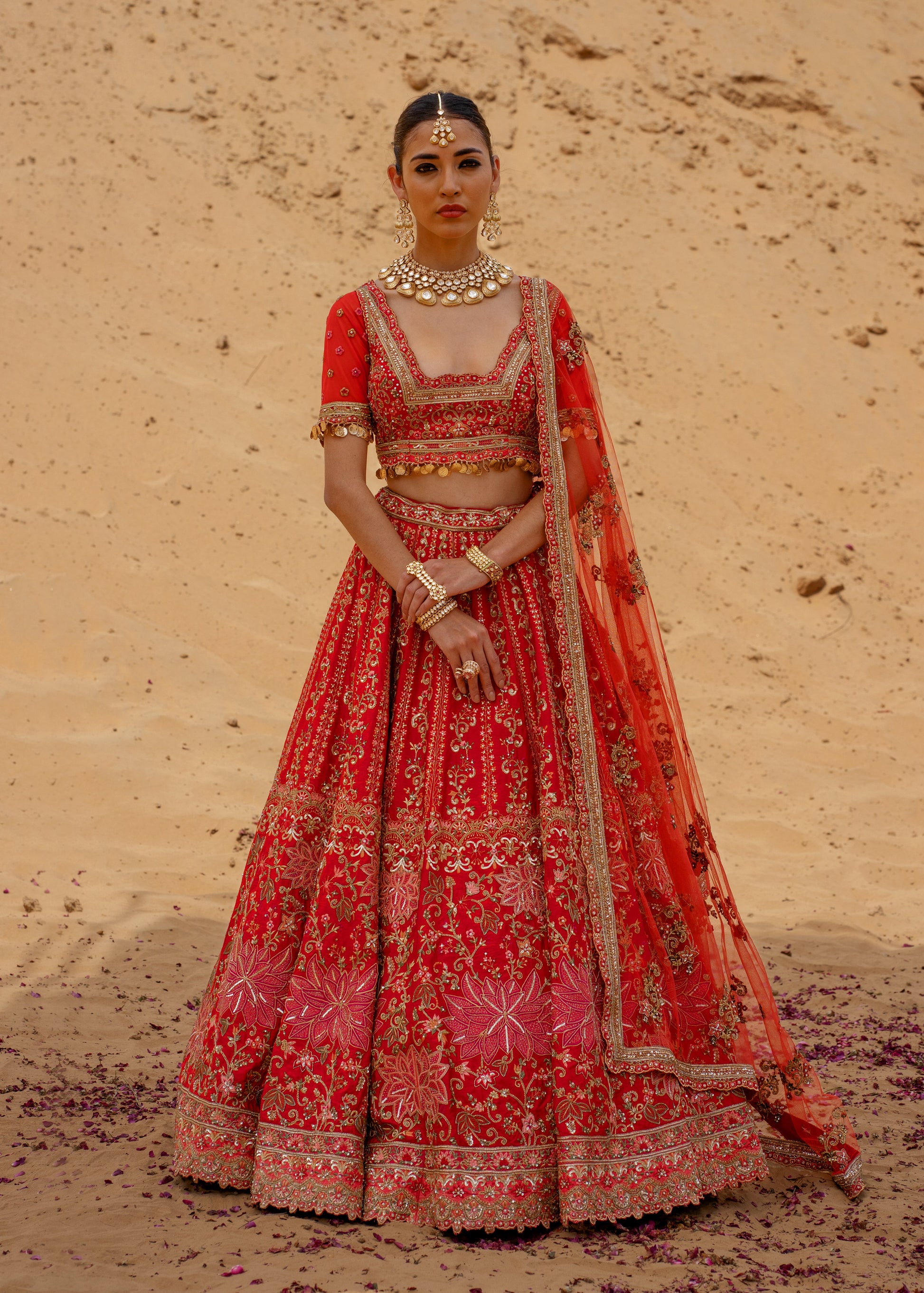 Woman in a traditional red embroidered outfit standing against a desert backdrop