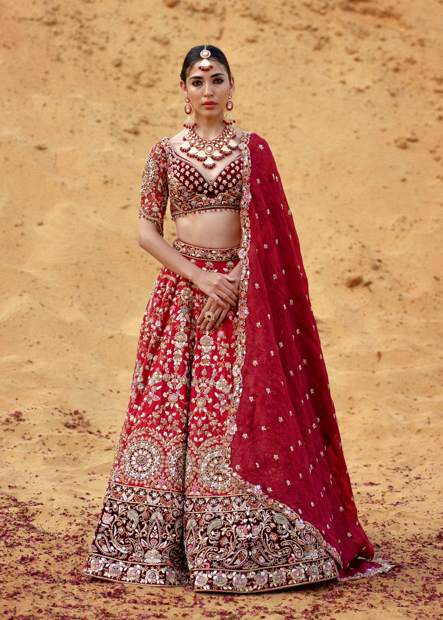 Woman in a traditional red and gold embroidered outfit against a desert backdrop