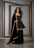 Woman in a black and gold traditional outfit standing in front of a mirror.