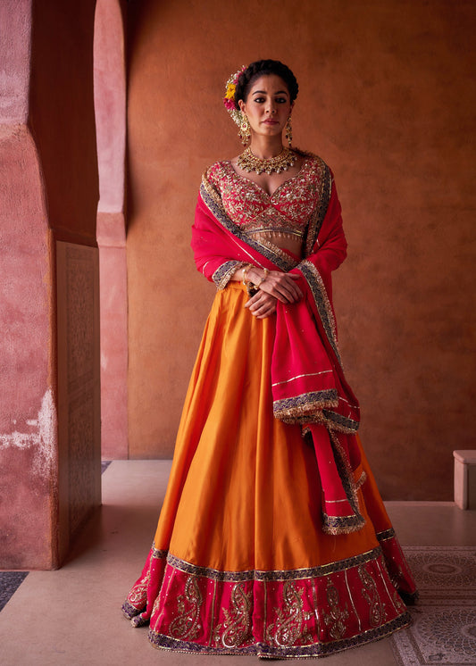Woman in a traditional red and orange outfit with intricate patterns against a warm-toned wall.