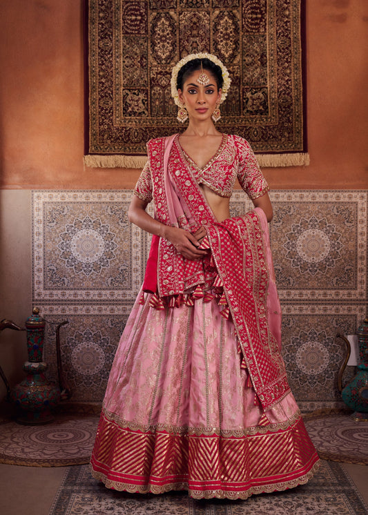 Woman in a traditional pink and red embroidered outfit standing in a room with patterned walls.