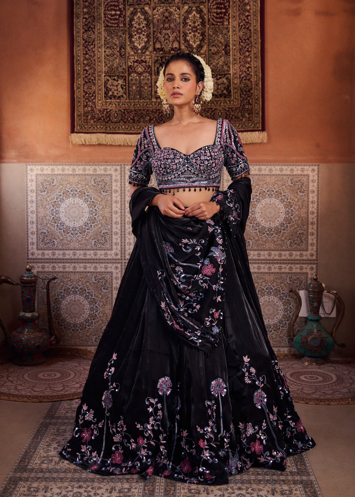 Woman in a black and floral traditional outfit standing in a decorated room.