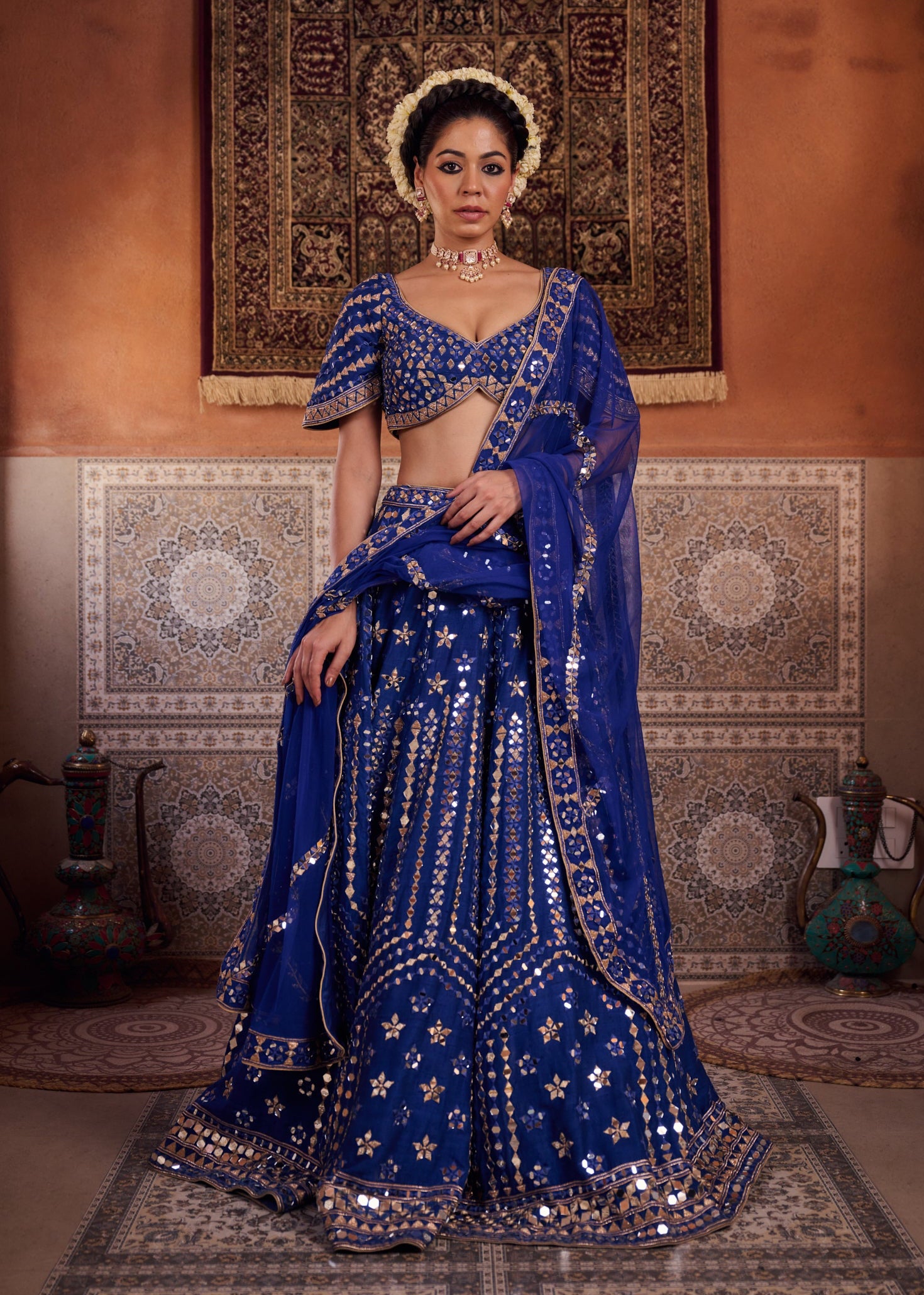 Woman in a traditional blue embroidered outfit standing in a decorated room.