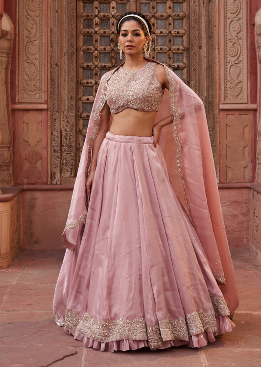 Woman in a traditional pink outfit standing in front of an ornate wooden door.