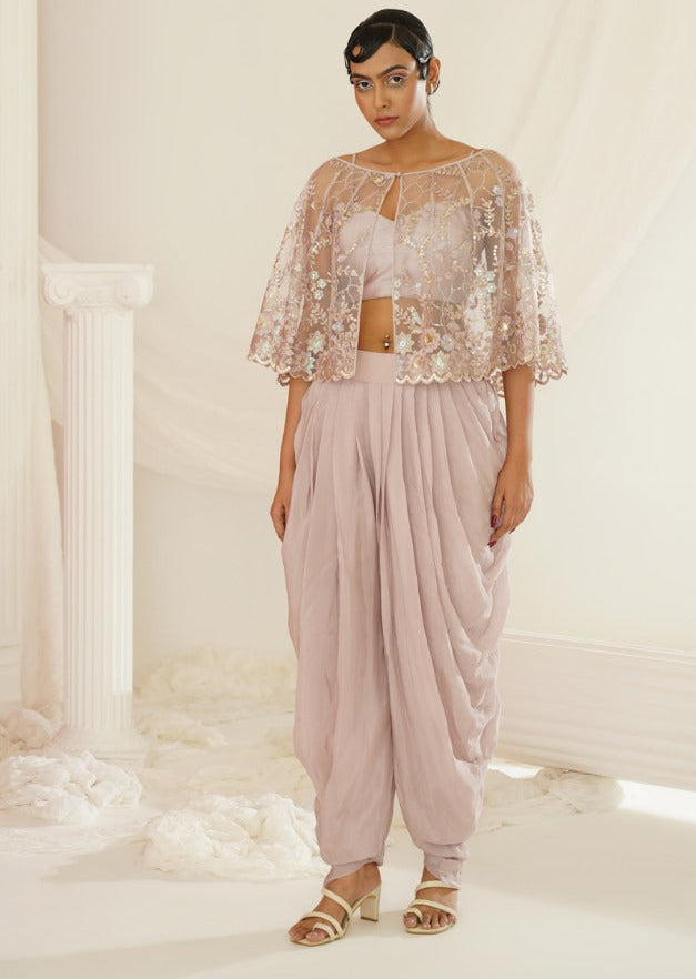 Woman wearing a floral top and light pink dhoti in a white room with classical columns.