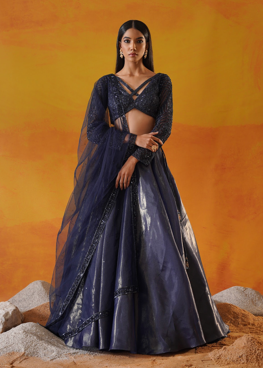 Woman in a dark blue traditional outfit standing against an orange background