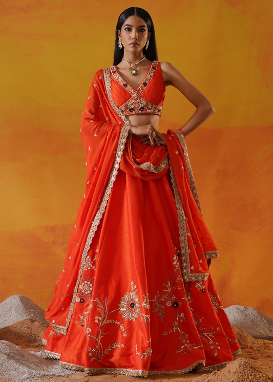 Woman in an orange traditional outfit with intricate designs against a warm-toned background