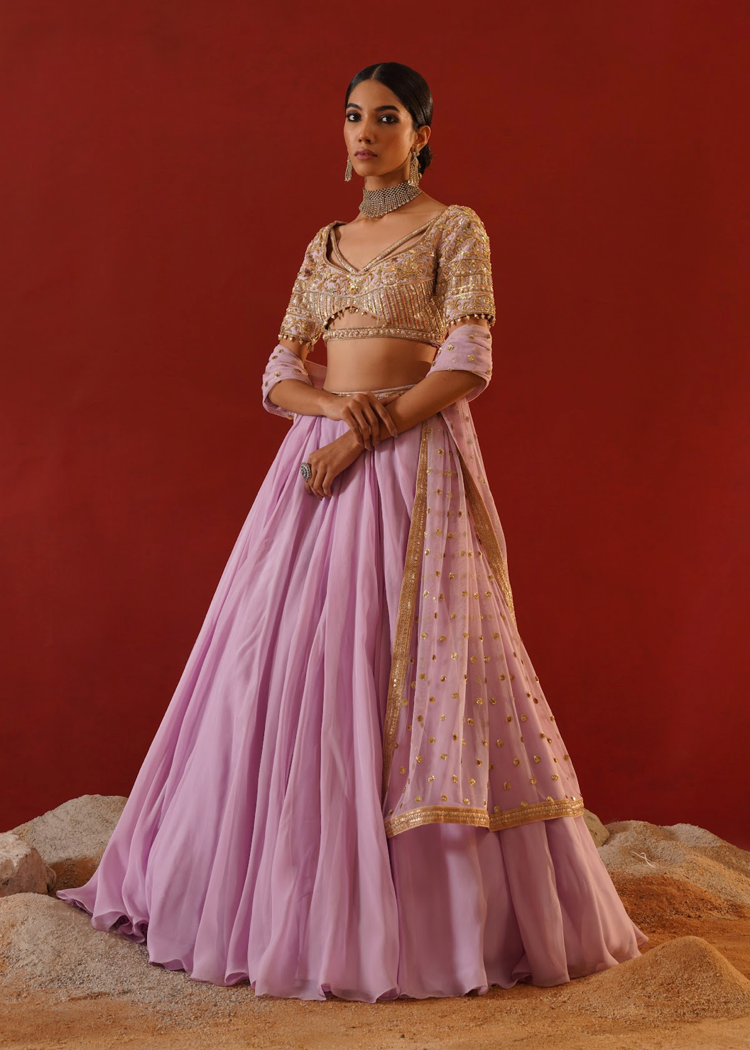 Woman in a traditional outfit with a pink skirt and gold top against a red background
