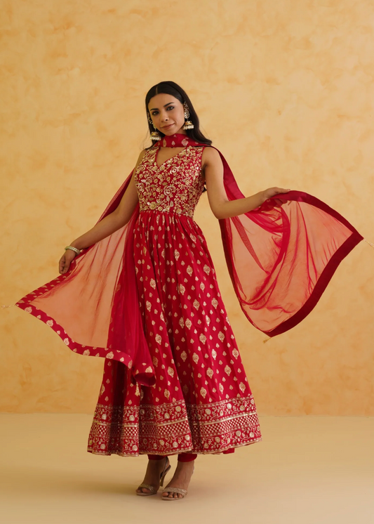 Woman wearing a red and pink traditional outfit with a matching dupatta against a beige background