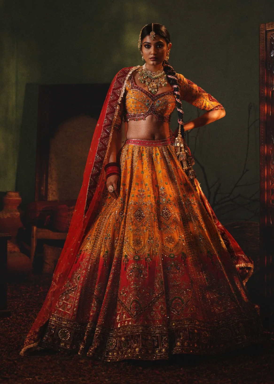Woman in traditional embroidered outfit with a red dupatta in a dimly lit room.