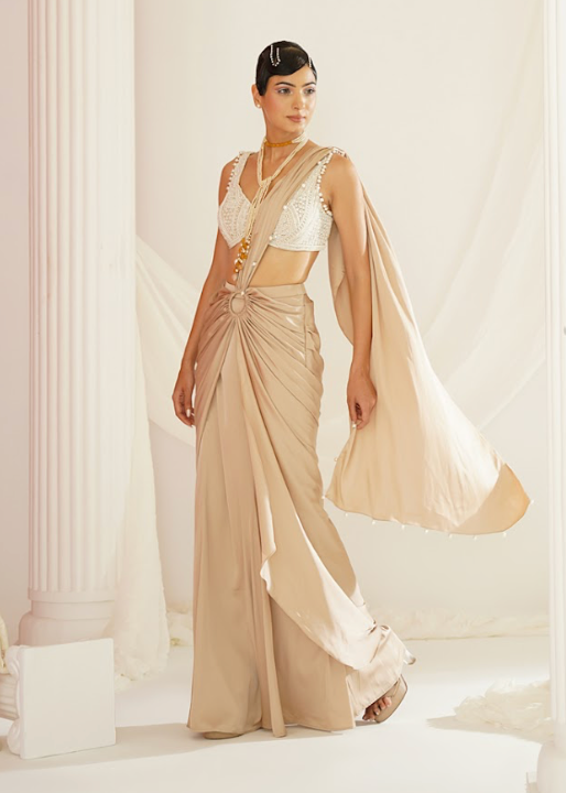 Woman in a beige saree standing in a classical setting with columns.