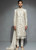 Man wearing a traditional embroidered sherwani with a matching dupatta against a gray background