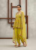 Woman in a yellow traditional outfit standing against a gray wall with wooden frames.
