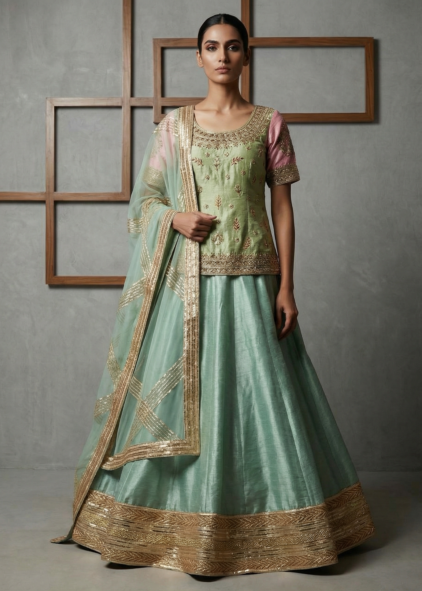 Woman wearing a light green traditional outfit with gold embroidery against a gray background