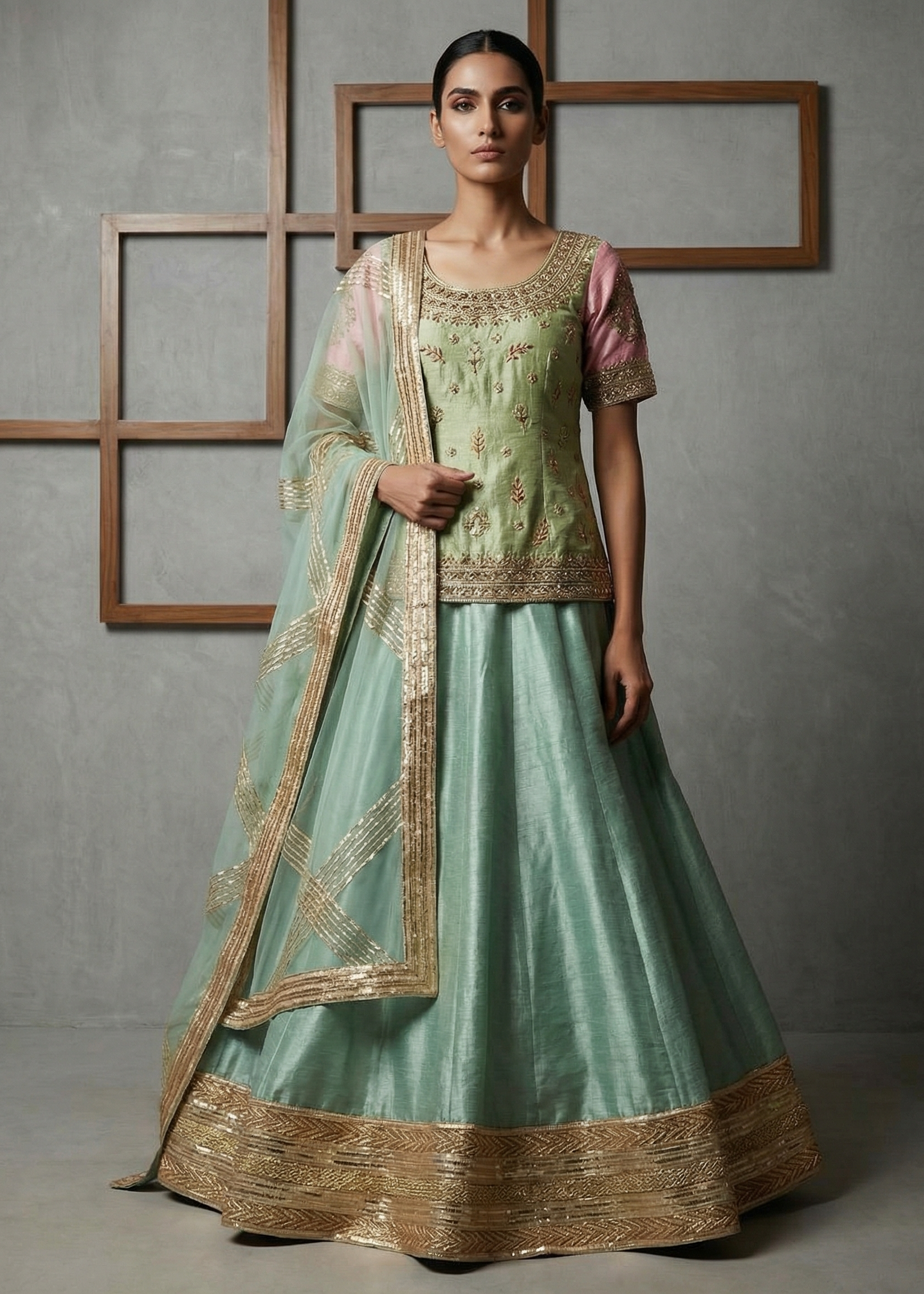 Woman wearing a light green traditional outfit with gold embroidery against a gray background