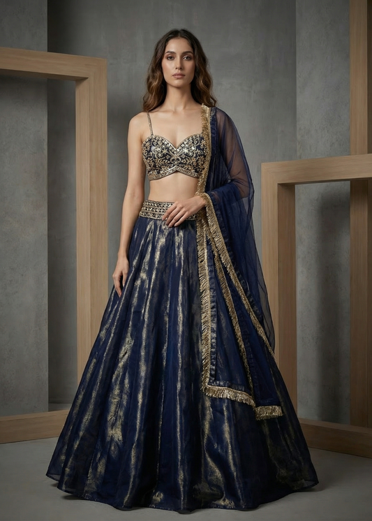 Woman wearing a traditional outfit with a dark blue lehenga and embroidered top against a neutral background.
