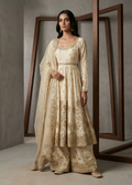 Woman wearing a traditional beige embroidered outfit standing in front of a mirror.
